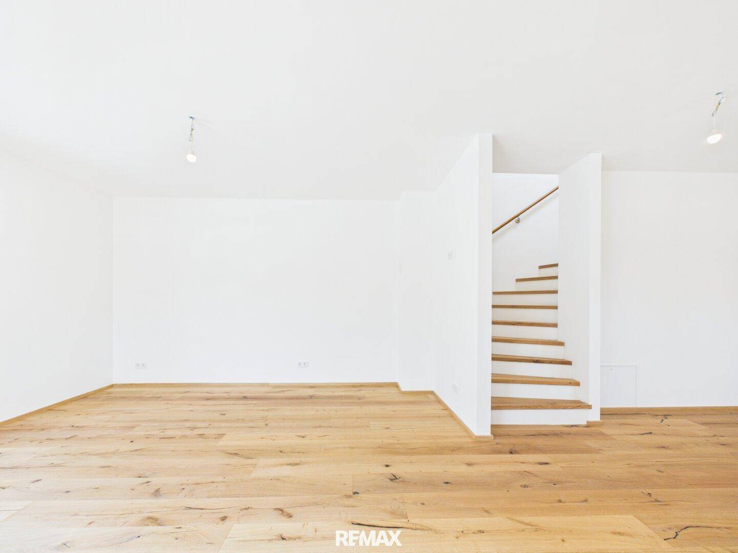 Heller Raum mit Echtholzboden, weißen Wänden und offener Holztreppe zum Obergeschoss.