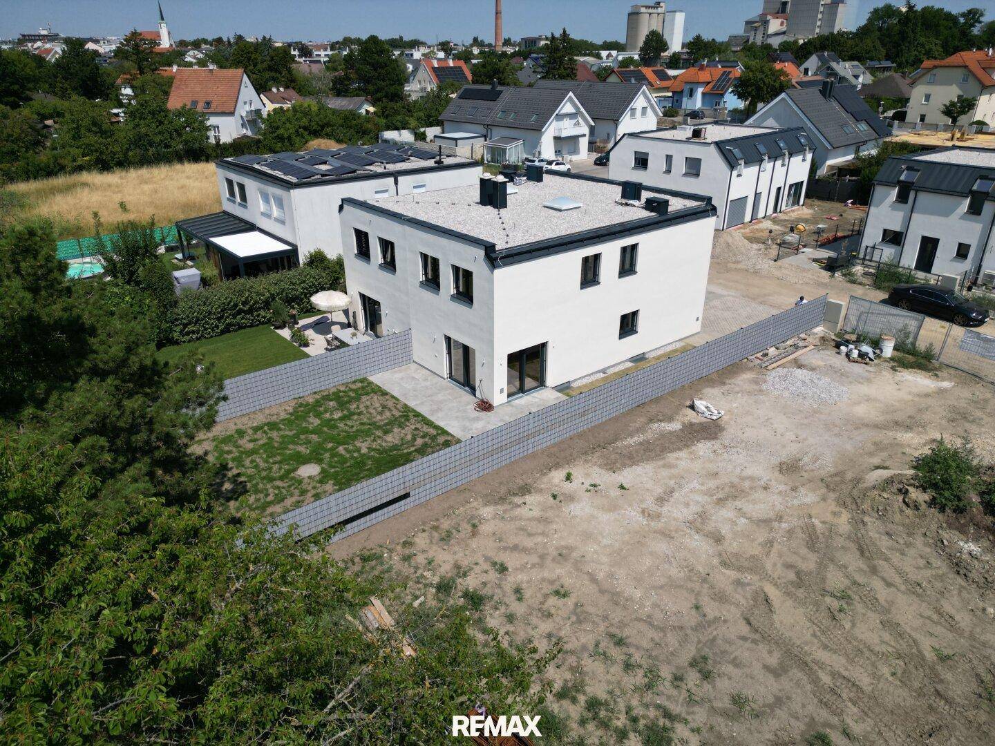 Moderne weiße Doppelhaushälfte mit Flachdach, kleinem Garten und angrenzendem unbebautem Grundstück.