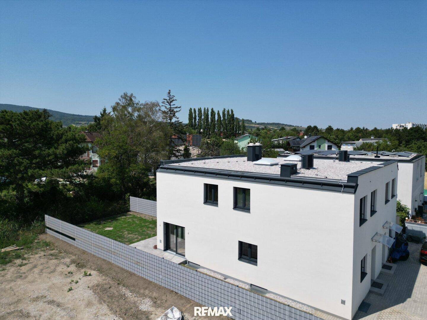 Moderne Doppelhaushälfte mit weißer Fassade, Flachdach und Blick auf die umliegende Landschaft.
