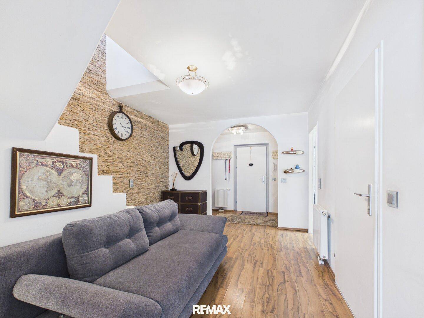 Gemütlicher Wohnbereich mit grauem Sofa, strukturierter Wand und Treppe, die in die obere Etage führt.