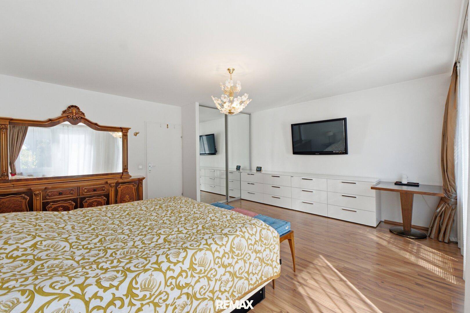 Geräumiges Schlafzimmer mit großem Bett, klassischer Holzkommode und Spiegel, hell und einladend.