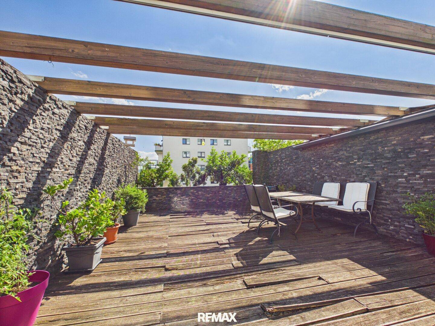 Sonniger Terrassenbereich mit Holzdeck und Steinmauern, bietet Platz für Outdoor-Möbel und Pflanzen.