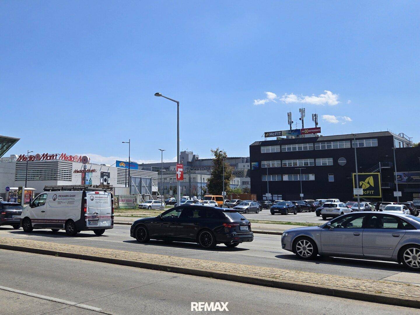 Belebte Straße mit Verkehr und Geschäftsgebäuden wie Media Markt und McFIT im städtischen Umfeld.