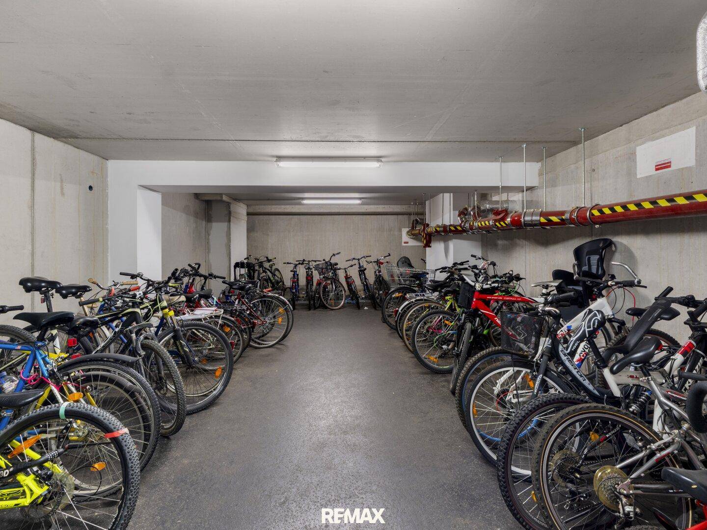 Gemeinschaftlicher Fahrradraum im Untergeschoss mit vielen abgestellten Fahrrädern und Betonwänden.