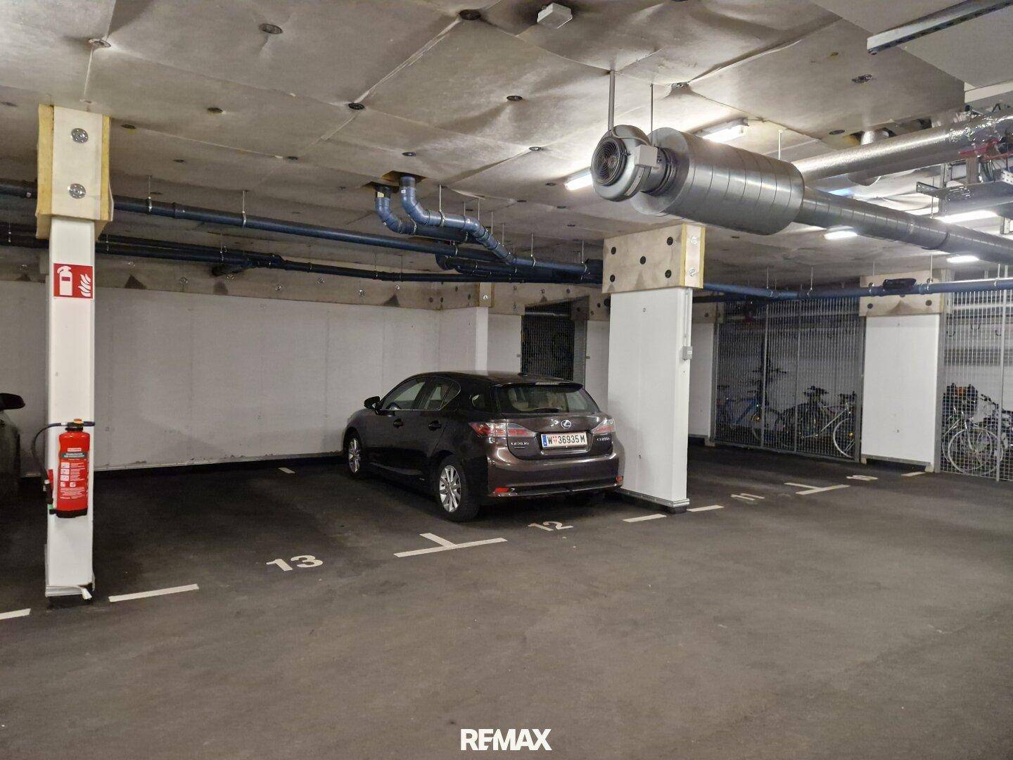 Tiefgaragenstellplatz mit einem geparkten Auto und sichtbaren Versorgungsleitungen.