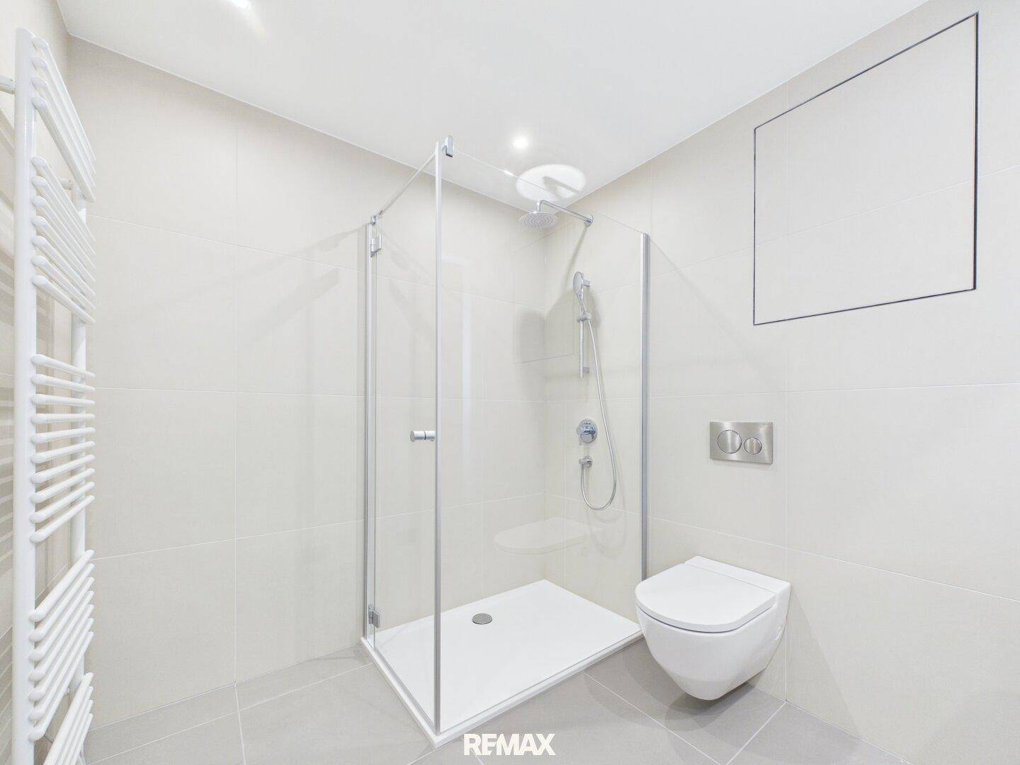 Modernes Badezimmer mit ebenerdiger Dusche, Wand-WC und beheiztem Handtuchhalter in hellen Farbtönen.