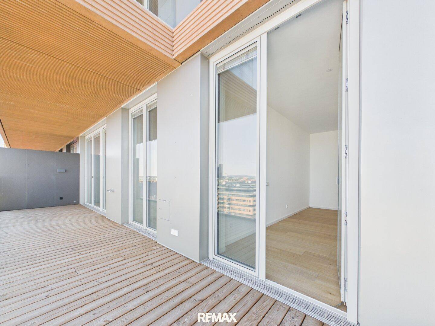 Geräumiger Balkon mit Holzboden und Zugang zu einem hellen Innenraum.