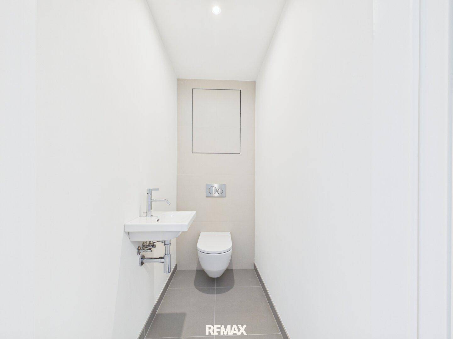 Kleines Gäste-WC mit modernem Waschbecken und Wand-WC, hell gefliest und minimalistisch gestaltet.