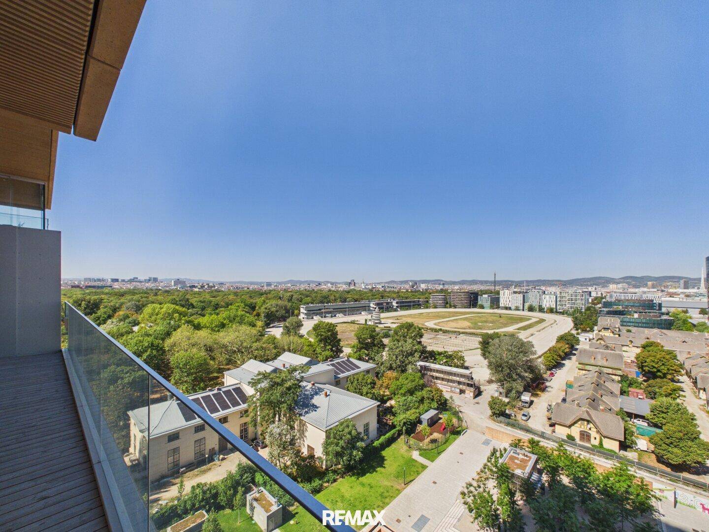 Balkon mit Glasbrüstung bietet weiten Blick auf Grünflächen und die Stadt.