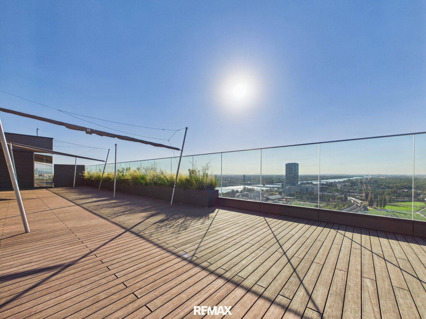 Geräumige Dachterrasse mit Holzboden, Glasbrüstung und sonnigem Stadtblick.