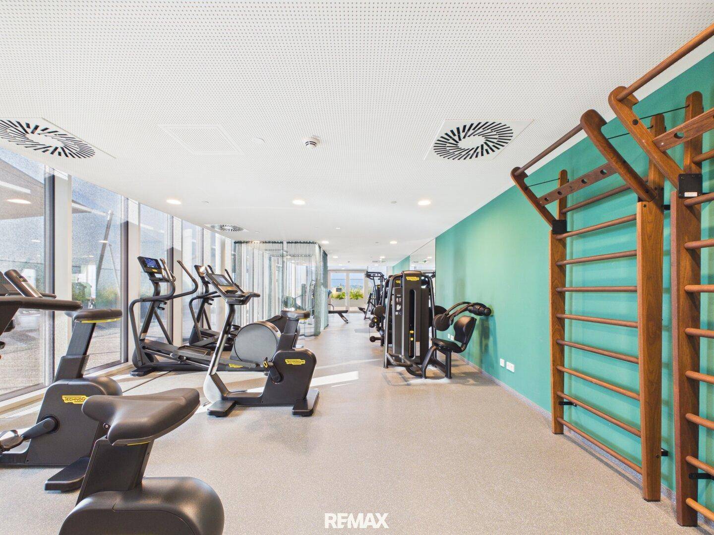 Moderner Fitnessraum mit verschiedenen Trainingsgeräten und großen Fenstern für natürliches Licht.