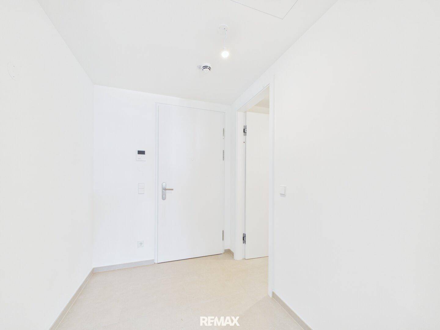 Heller Eingangsbereich einer Wohnung mit weiß gestrichenen Wänden und Fliesenboden.
