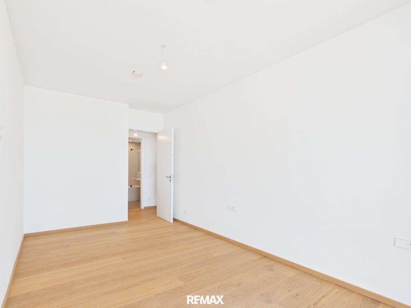 Helles Schlafzimmer mit Parkettboden und Zugang zu einem modernen Badezimmer.