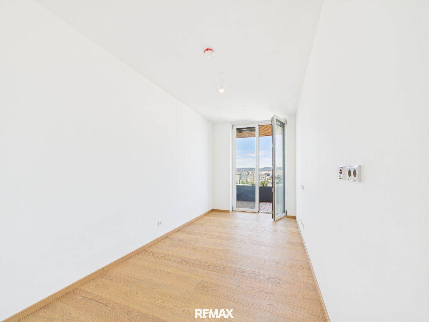 Helles Schlafzimmer mit Parkettboden und geöffneter Balkontür, die frische Luft hereinlässt.