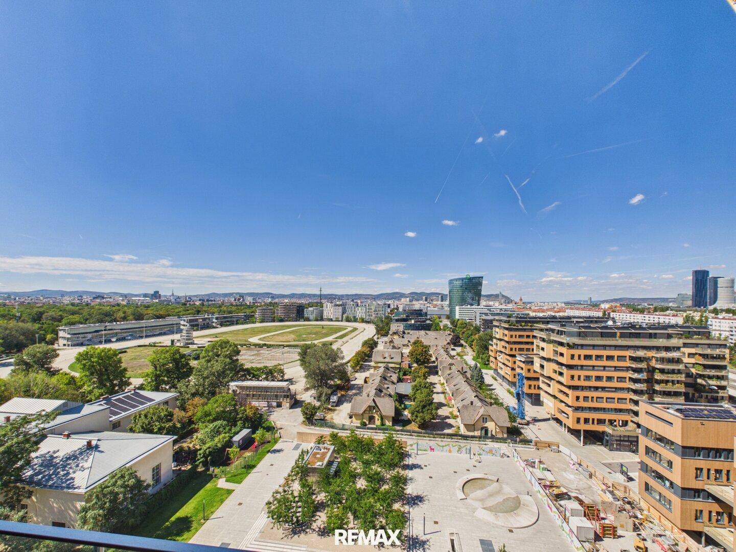 Weitläufiger Blick über die Stadt mit Grünflächen, Gebäuden und einem Skatepark.