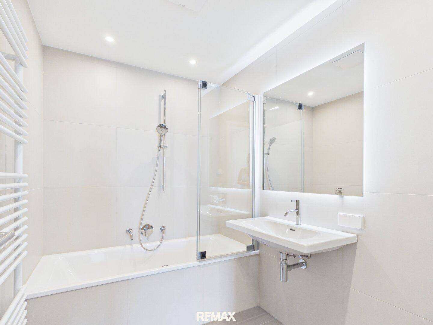 Modernes Badezimmer mit Badewanne, Duschabtrennung und beleuchtetem Spiegel.