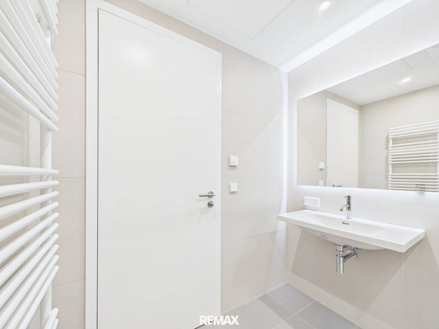 Modernes Badezimmer mit Waschtisch, beleuchtetem Spiegel und Handtuchheizkörper.