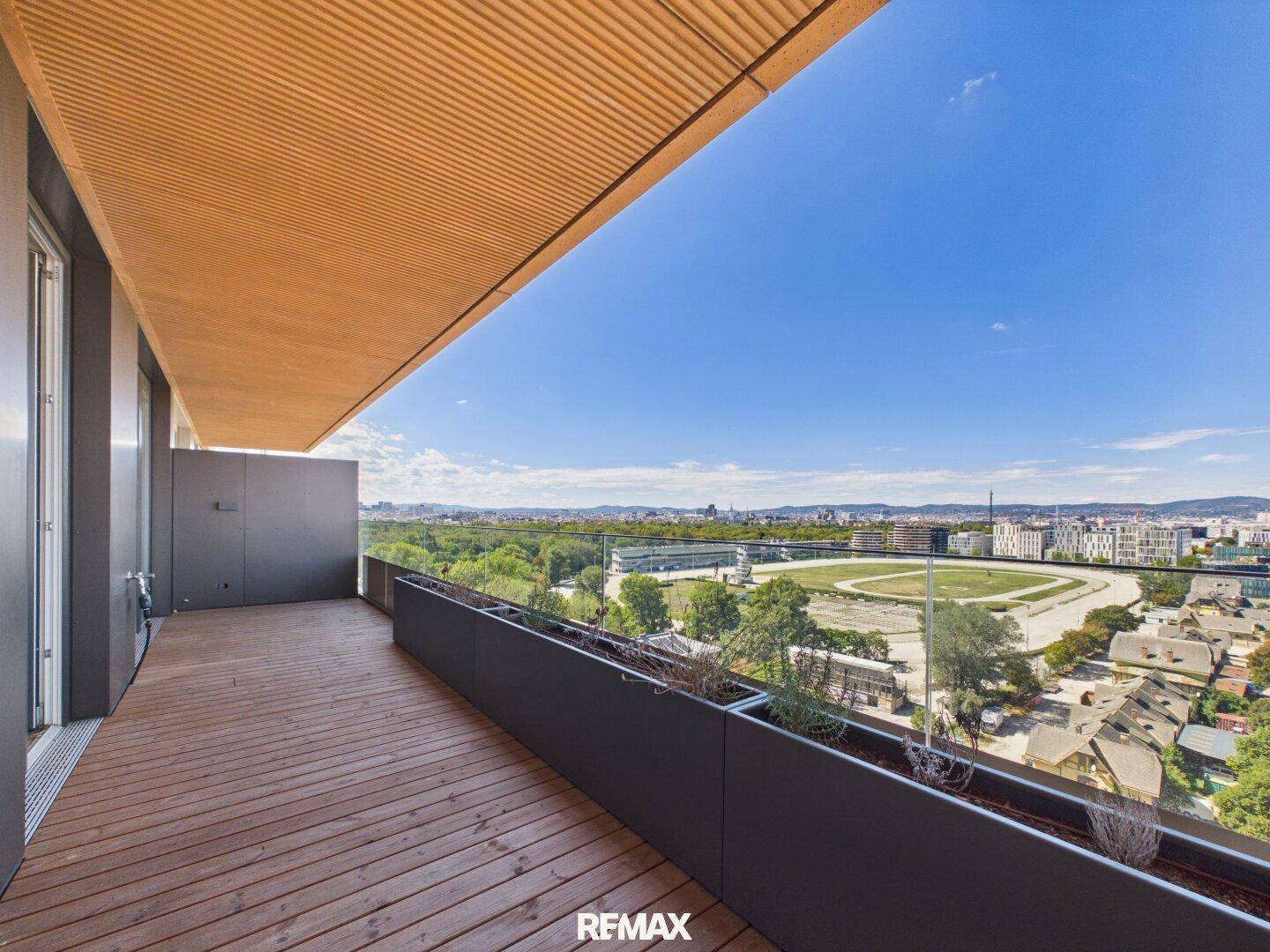 Großer Balkon mit Holzboden und weitem Blick über die Stadt und die grüne Umgebung.