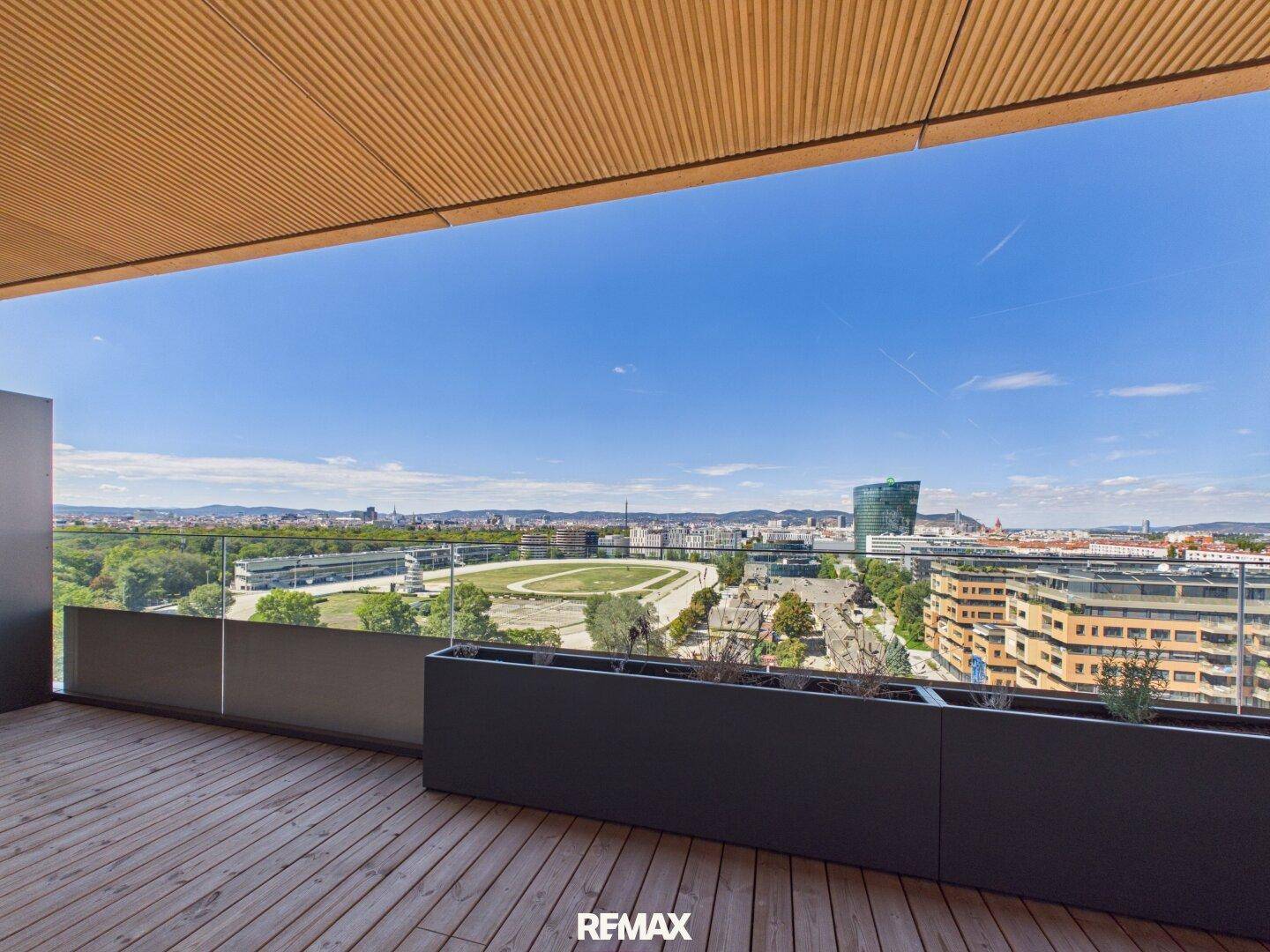 Geräumiger Balkon mit Holzboden und weitem Blick über die Stadt und eine Rennbahn.