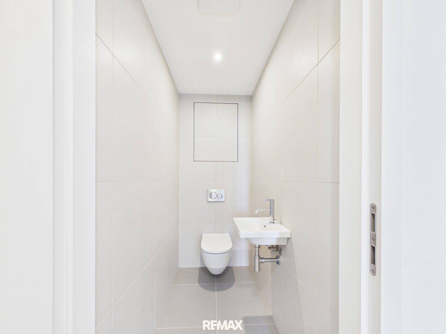 Separates Gäste-WC mit wandhängender Toilette und kleinem Handwaschbecken.