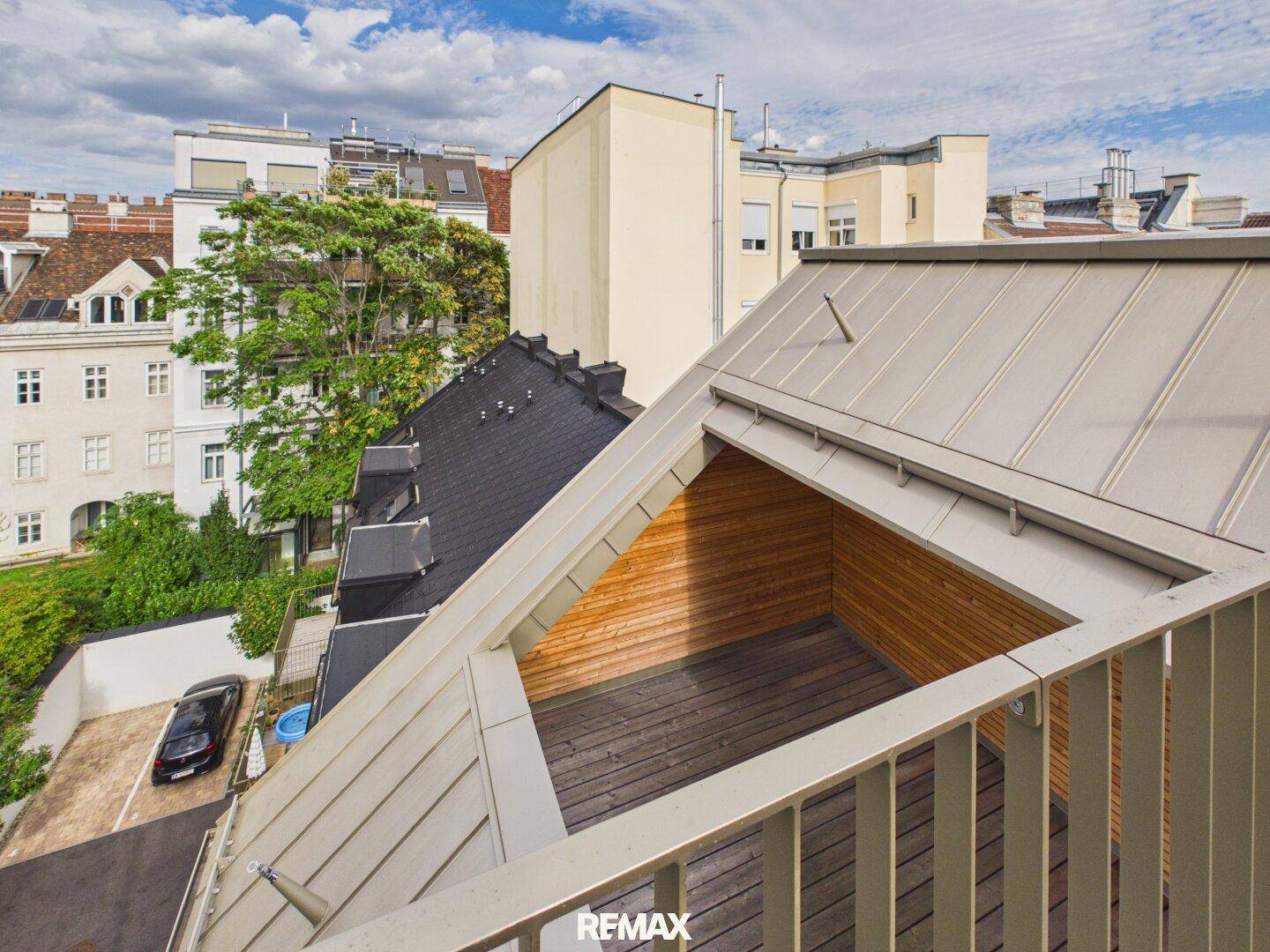 Blick von oben auf die Dachterrasse mit Holzboden und die Dächer der umliegenden Gebäude.