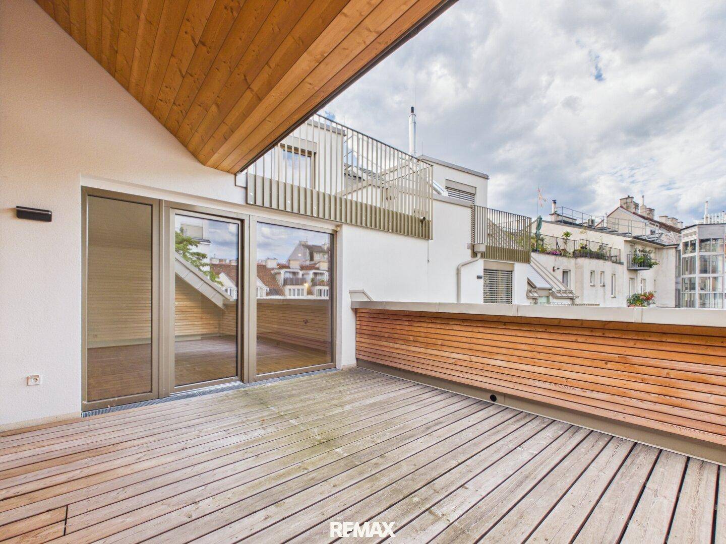 Breite Dachterrasse mit Holzboden und Holzverkleidung, zugänglich durch große Glastüren.