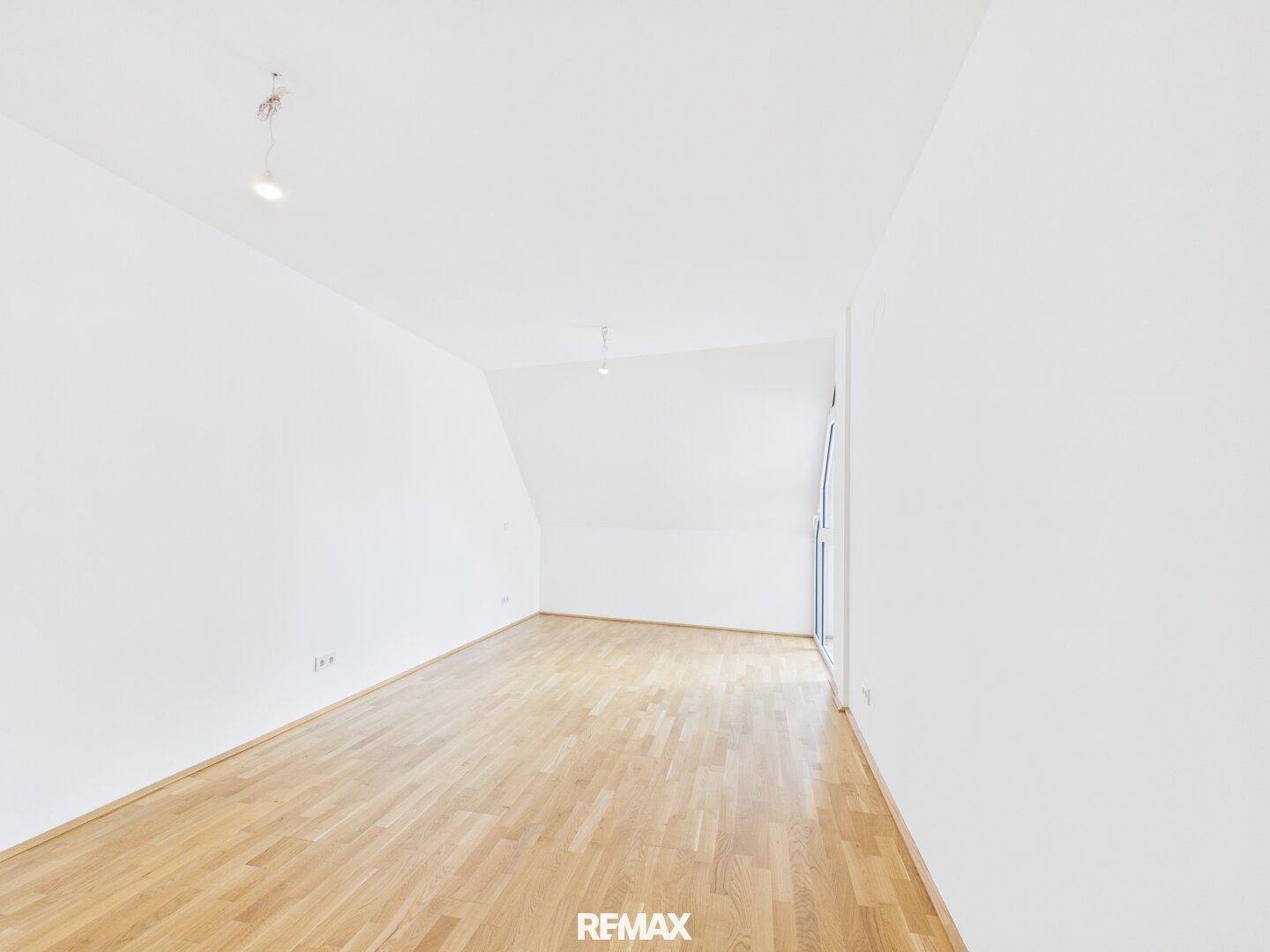 Helles, leeres Zimmer im Dachgeschoss mit schräger Decke und Parkettboden, ideal als Schlafzimmer.
