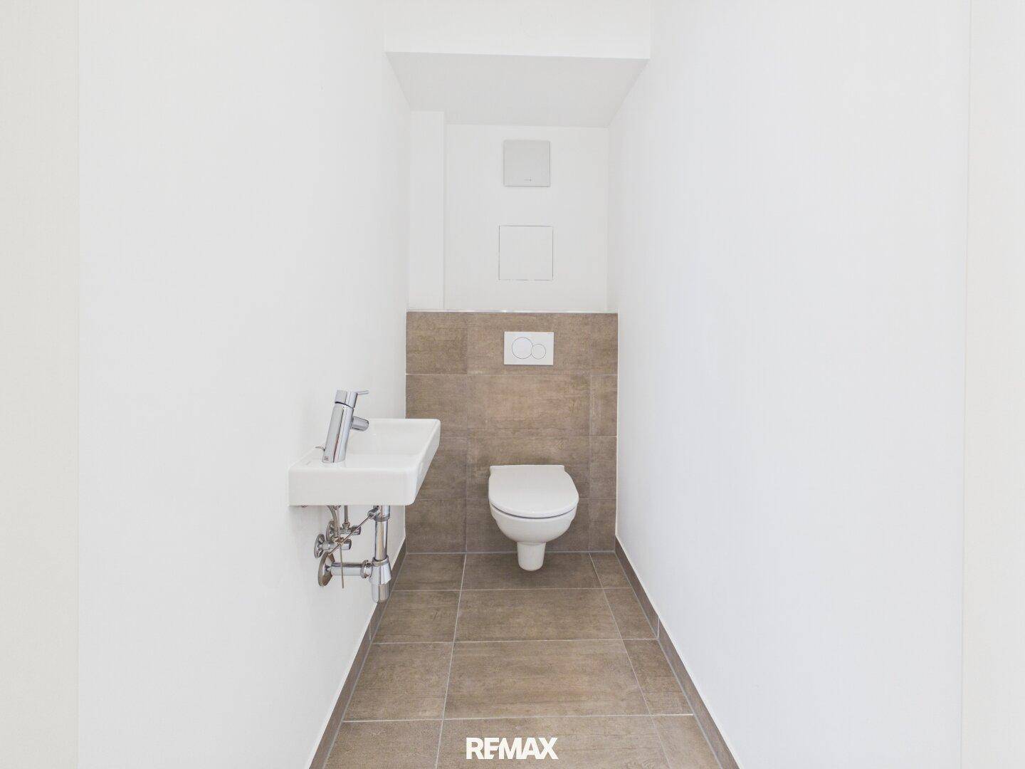 Modernes Gäste-WC mit Wand-WC, kleinem Waschbecken und grauen Fliesen an der Wand.