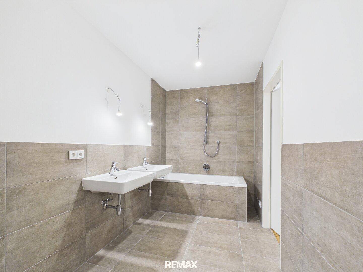 Modernes Badezimmer mit Badewanne, Doppelwaschbecken und grauen Fliesen an Wänden und Boden.