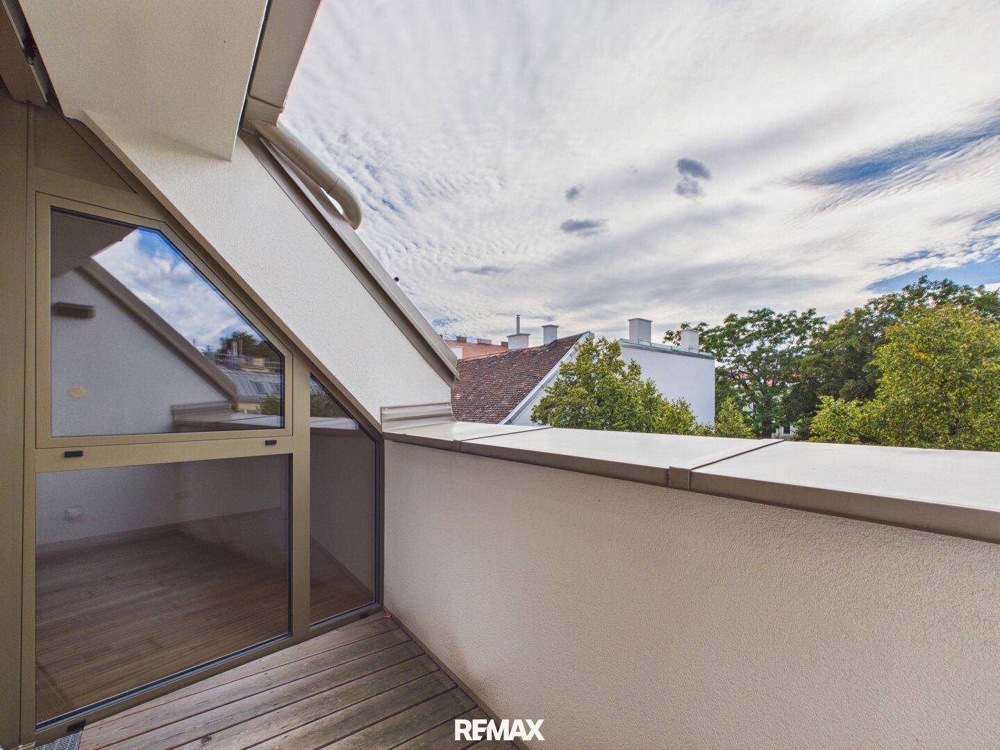 Kleiner Balkon mit Holzboden und schräger Dachkonstruktion, bietet einen Blick auf die Umgebung.