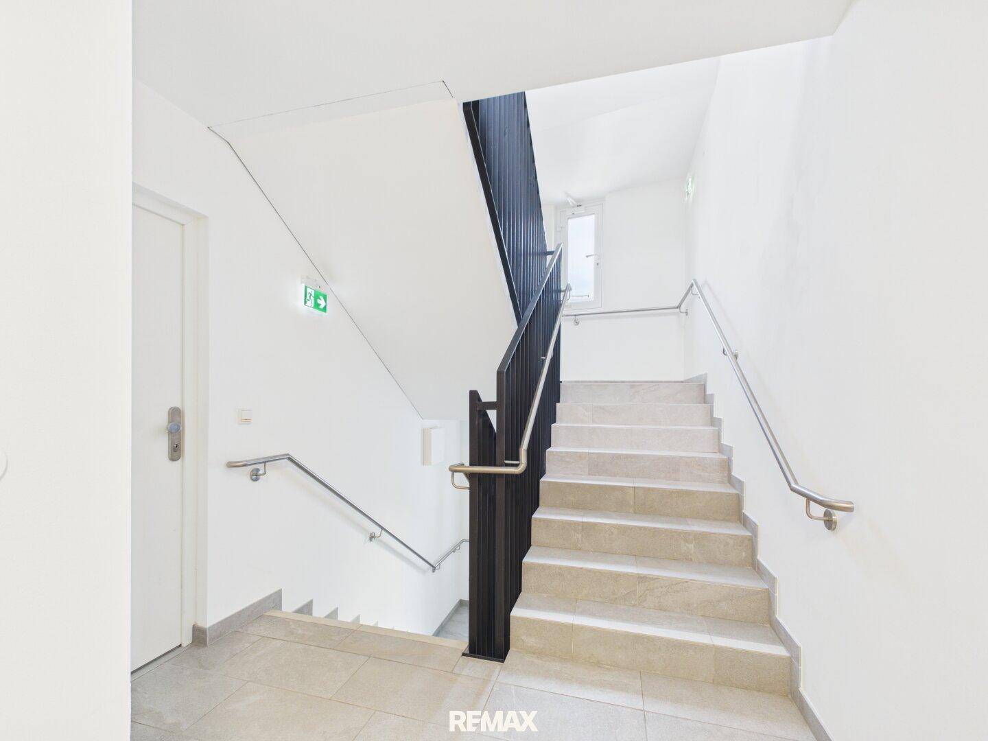 Helles Treppenhaus mit Steinstufen und modernen Metallgeländern in einem Mehrfamilienhaus.