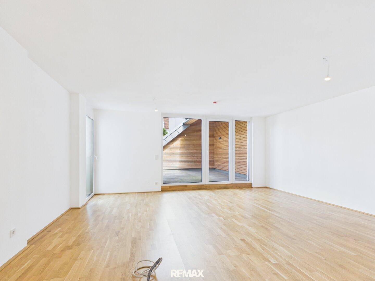 Geräumiges, helles Wohnzimmer mit Parkettboden und großen Fenstern, die zur Terrasse führen.
