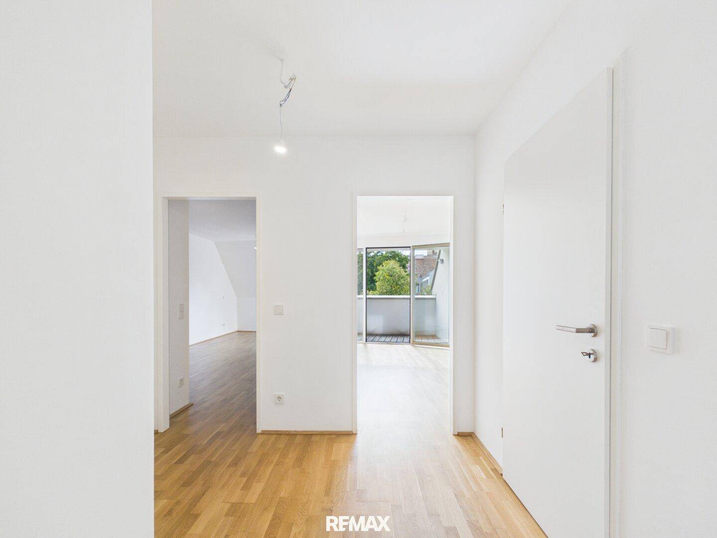 Heller Eingangsbereich mit Parkettboden, der zu verschiedenen Zimmern und einem Balkon führt.
