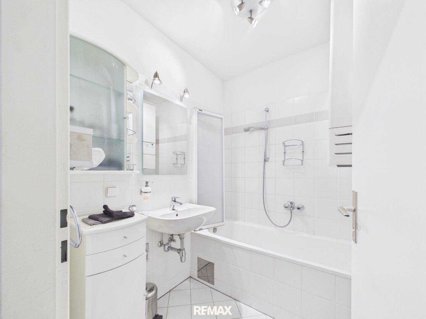 Helles Badezimmer mit Badewanne, Dusche, weißen Fliesen und Spiegelschrank.