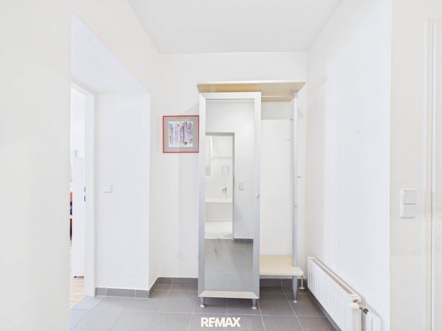 Heller Flur mit Fliesenboden, Garderobe und Spiegel, der zu anderen Räumen führt.