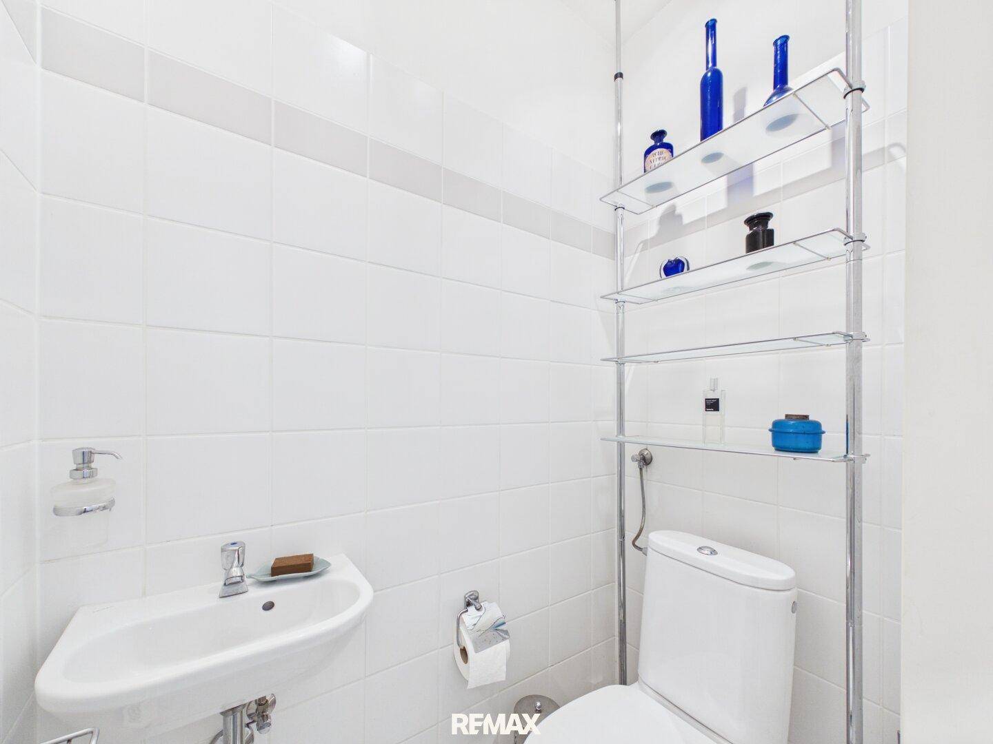 Kleines Gäste-WC mit Wand-WC, Waschbecken und praktischen Ablageregalen.