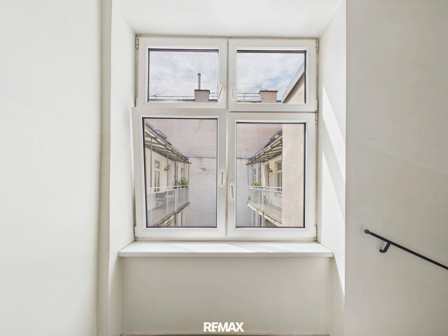 Fenster im Treppenhaus mit Blick auf den Innenhof und die umliegenden Balkone.