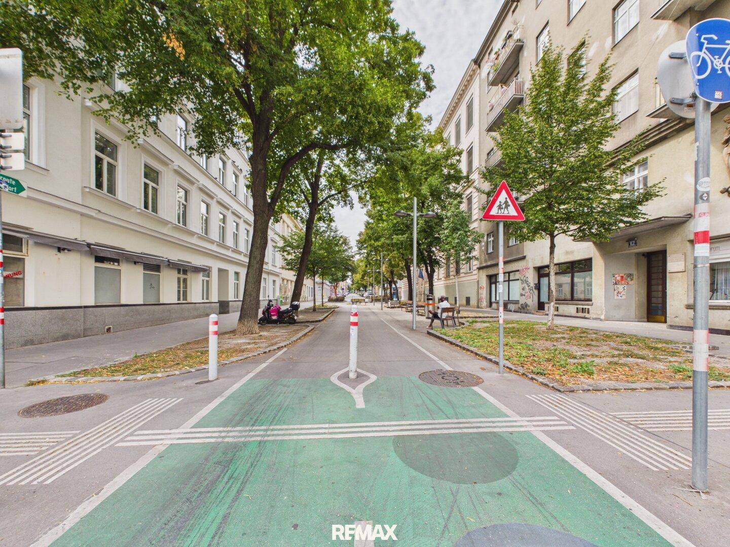Grüne Fahrradstraße mit Bäumen und Gebäuden in einer städtischen Umgebung.