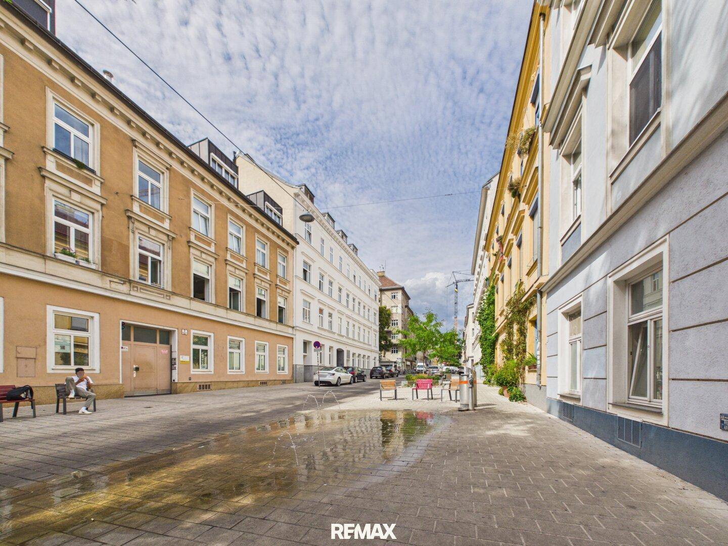 Stadtansicht mit historischen Gebäuden, Bäumen und einem sonnigen Gehweg.