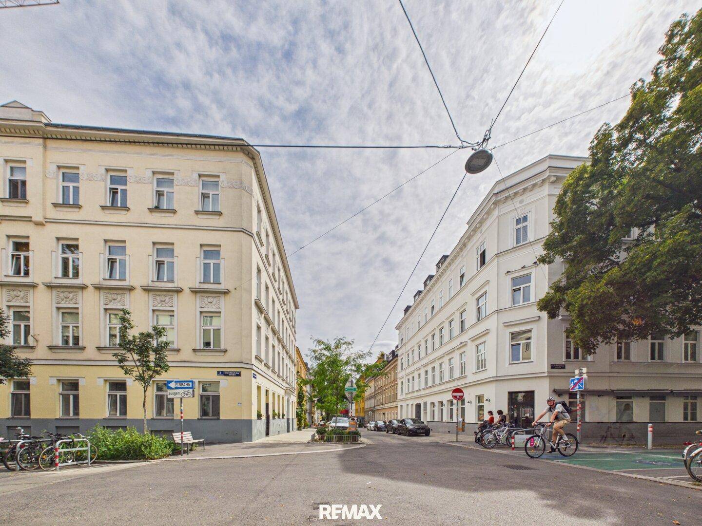 Kreuzung in der Stadt mit Gebäuden, Bäumen und Fahrrädern im urbanen Umfeld.
