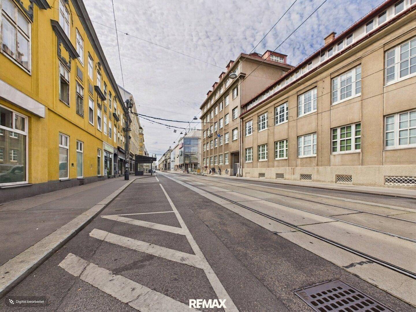 Stadtstraße mit Straßenbahnschienen, historischen Gebäuden und bewölktem Himmel.