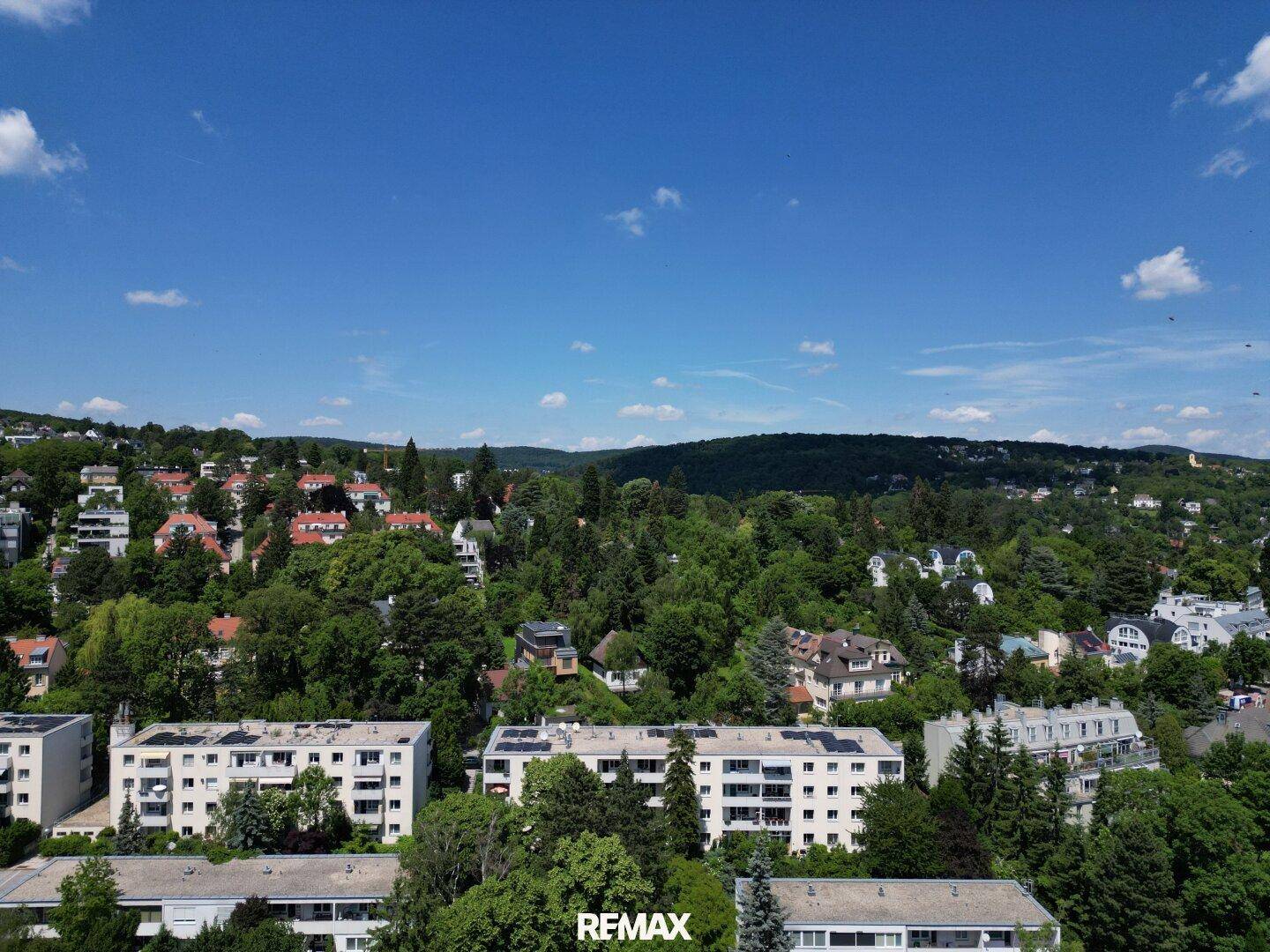 Weitläufige Ansicht der grünen Umgebung mit Wohngebäuden und Hügeln im Hintergrund.