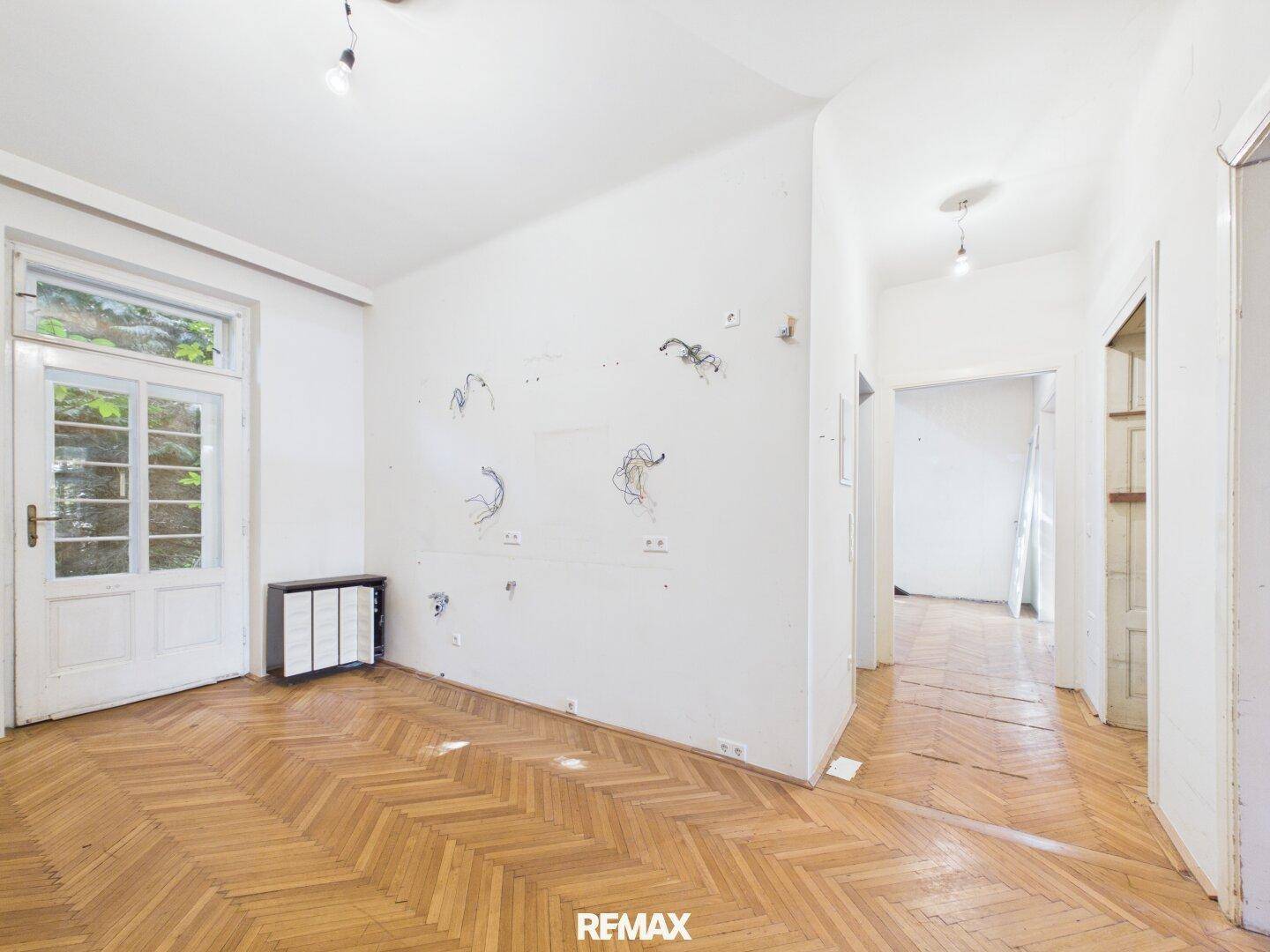 Geräumiges Zimmer mit Fischgrätparkett und Zugang zur Außentür, ideal für Wohnzwecke.