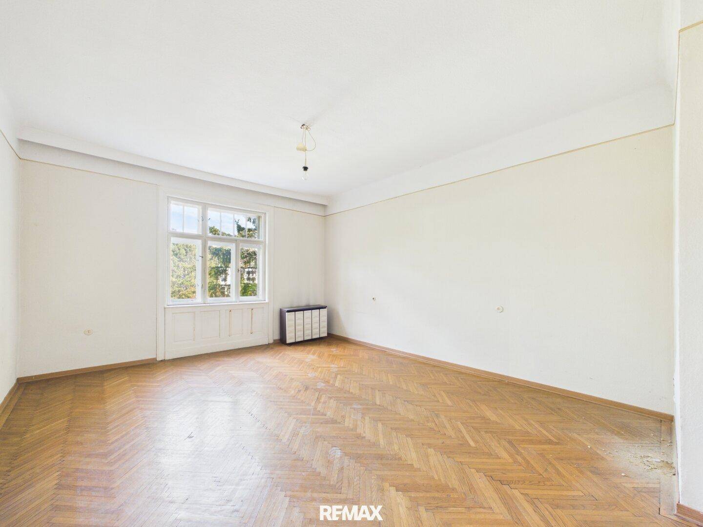 Geräumiges Wohnzimmer mit Fischgrätparkett und großem Fenster, bereit zur individuellen Gestaltung.