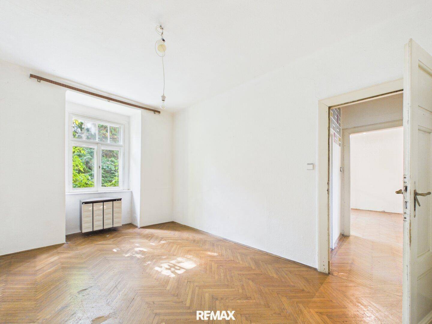 Helles Zimmer mit Fischgrätparkett und großem Fenster, ideal für ein Schlaf- oder Arbeitszimmer.