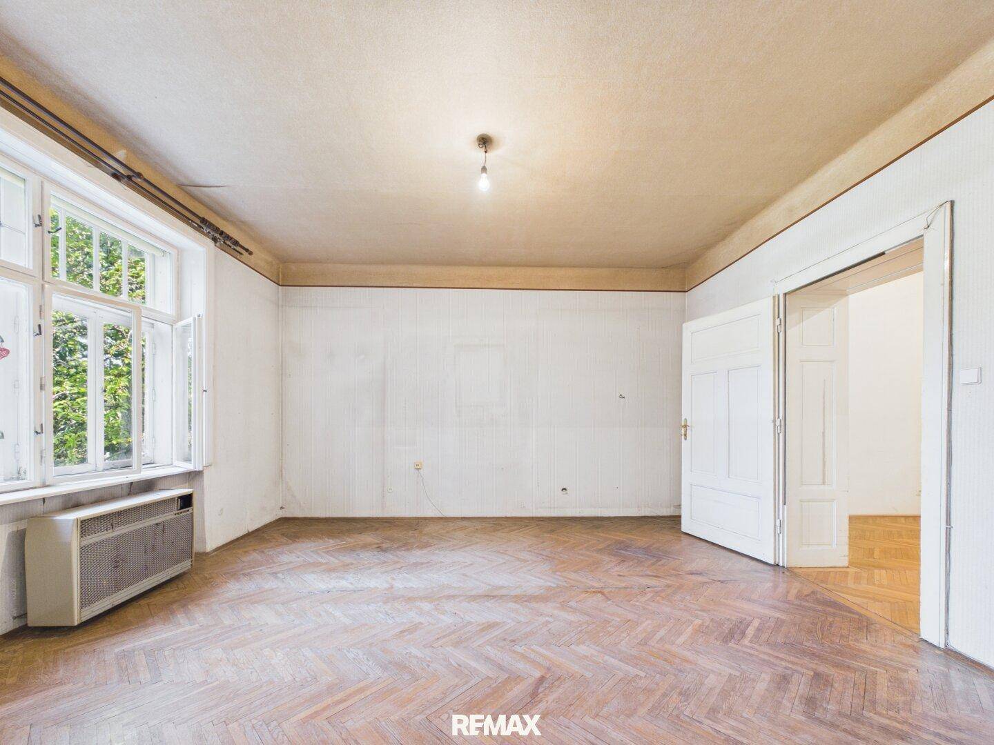 Helles Wohnzimmer mit Fischgrätparkett und großem Fenster, bereit für eine Modernisierung.