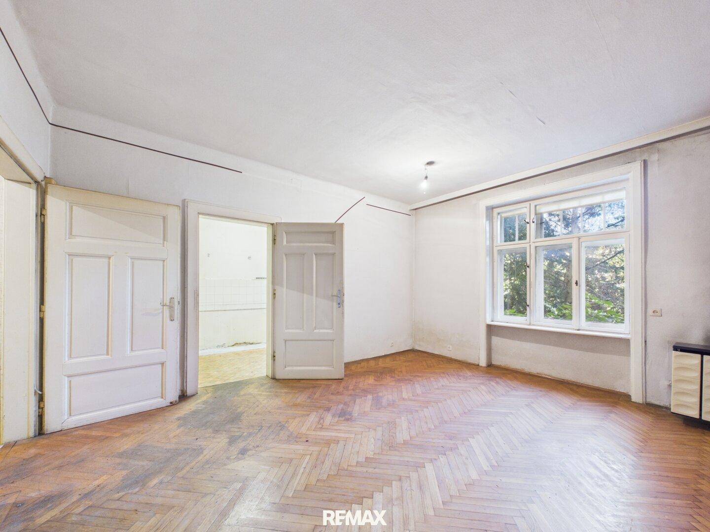 Geräumiges Zimmer mit Fischgrätparkett und großen Fenstern, ideal für eine Neugestaltung.