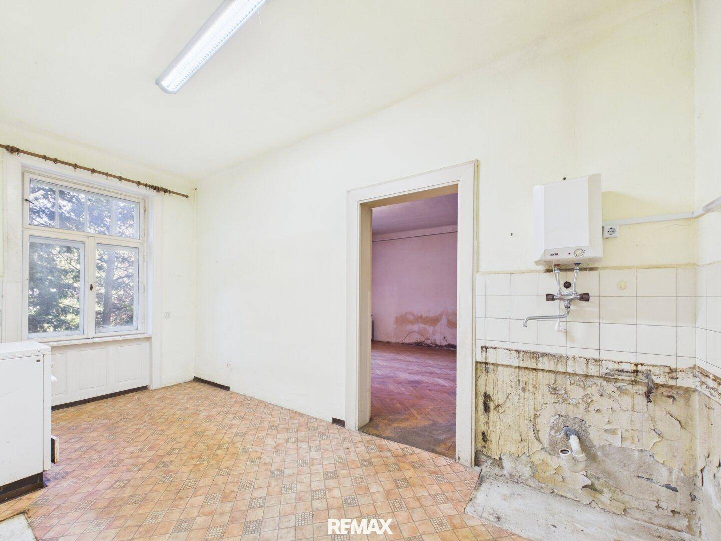 Renovierungsbedürftige Küche mit Fliesenboden, Fenster und Gastherme an der Wand.