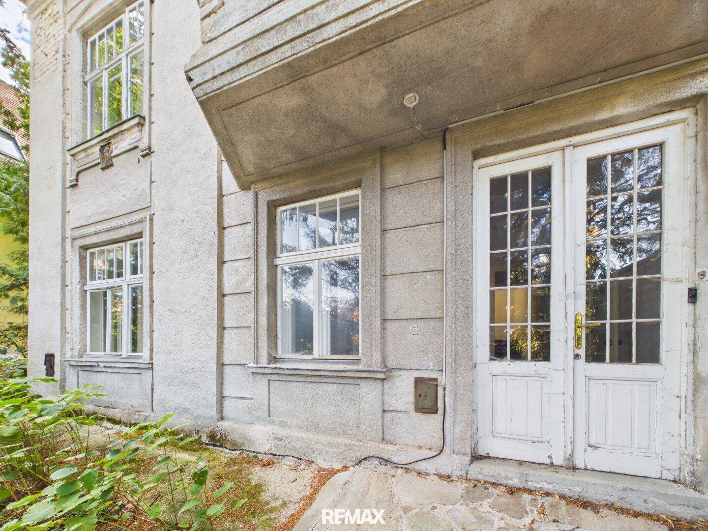 Detailansicht der Gebäudefassade mit alten Fenstern und einer Doppeltür, die zum Garten führt.
