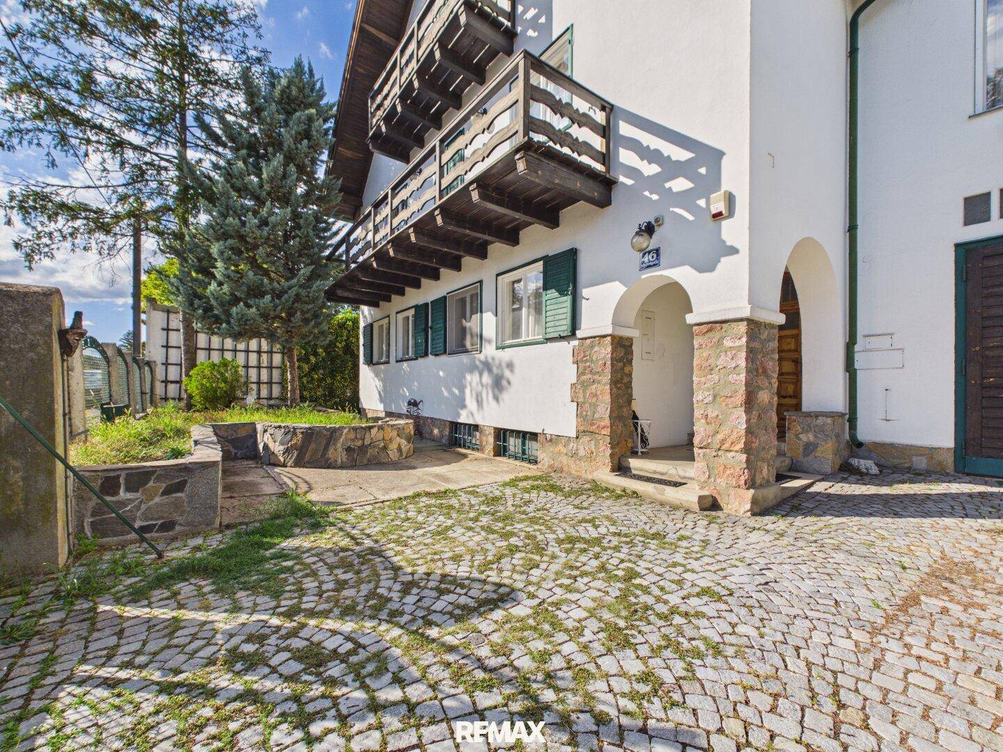 Eingangsbereich des Hauses mit gepflasterter Auffahrt, Steinsäulen und einem kleinen Blumenbeet.